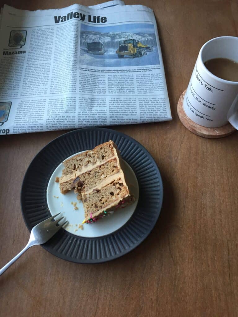 a piece of sticky toffee apple cake on a plate with newspaper and cup of coffee.