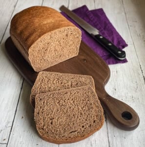 a loaf of sweet brown bread on a cutting board with two slices, knife, and napkin.