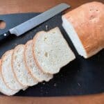 a loaf of sweet Portuguese bread with several slices and a bread knife on a cutting board