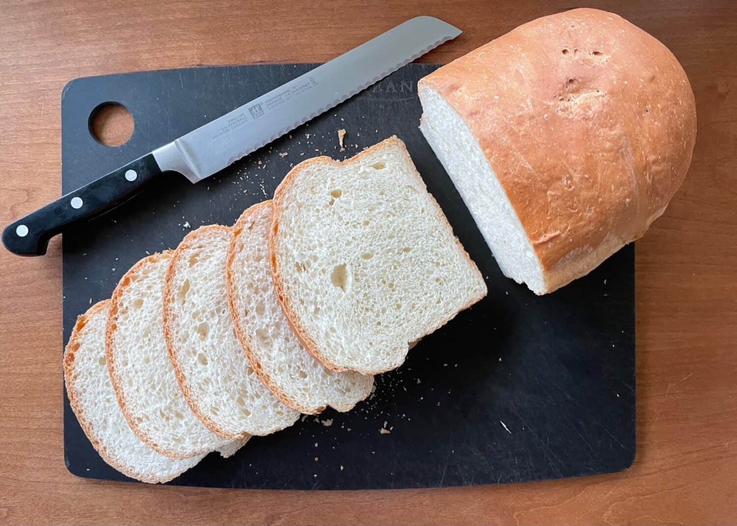 loaf of sweet Portuguese bread with several slices and a bread knife on a cutting board.
