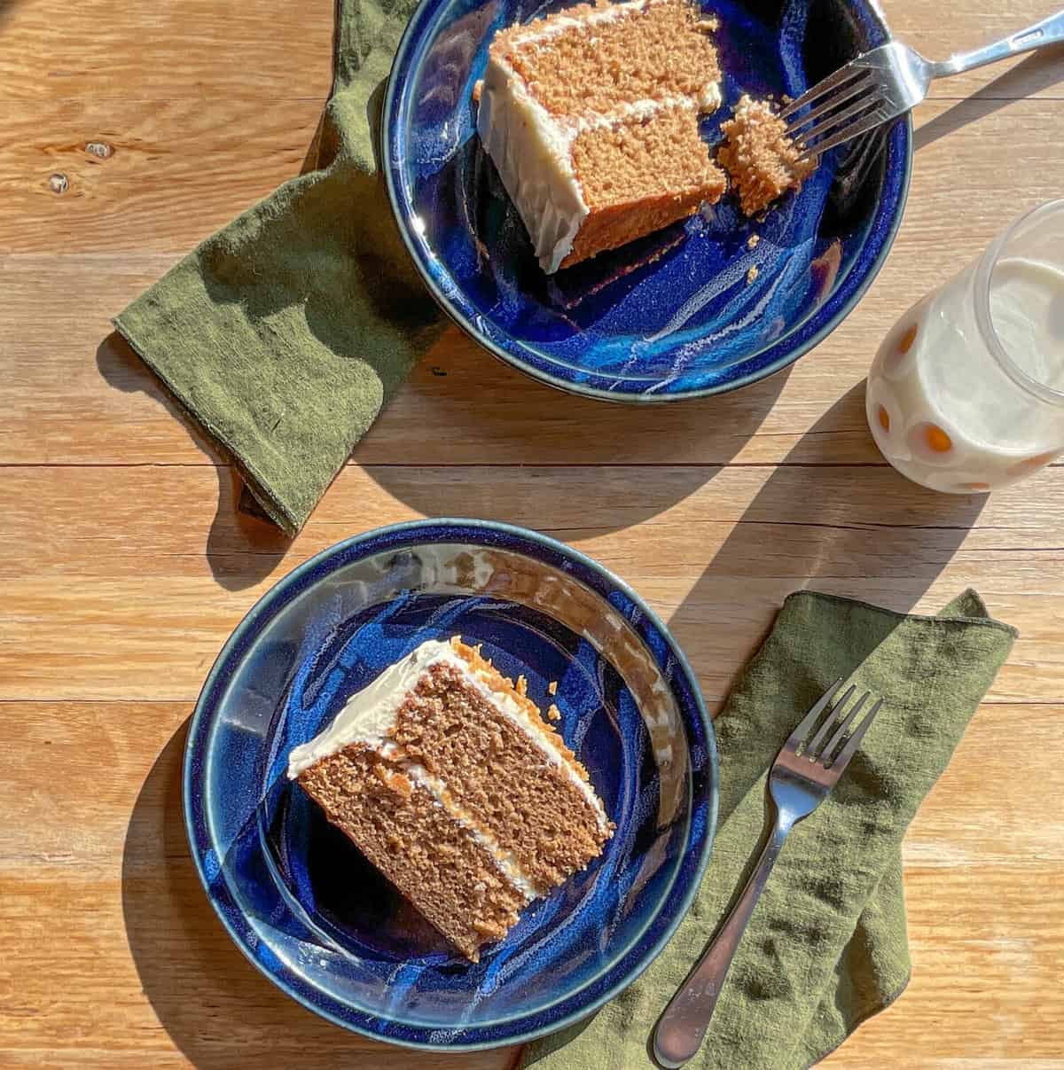 two pieces of applesauce cake on plates with forks and a milk glass.