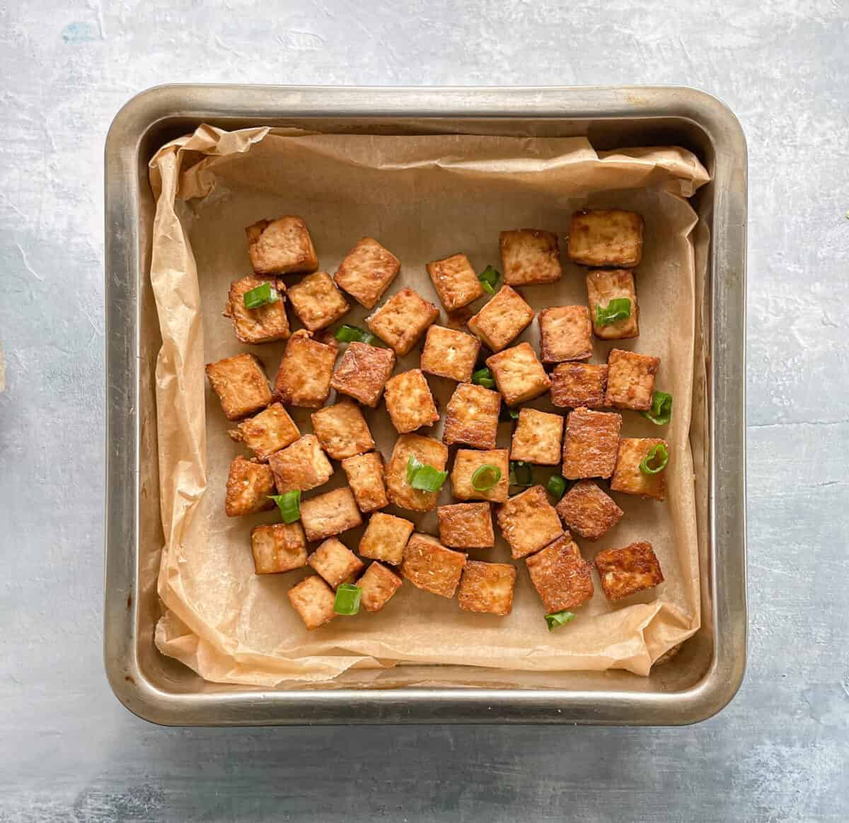 pan of crispy baked tofu in parchment garnished with green onions.