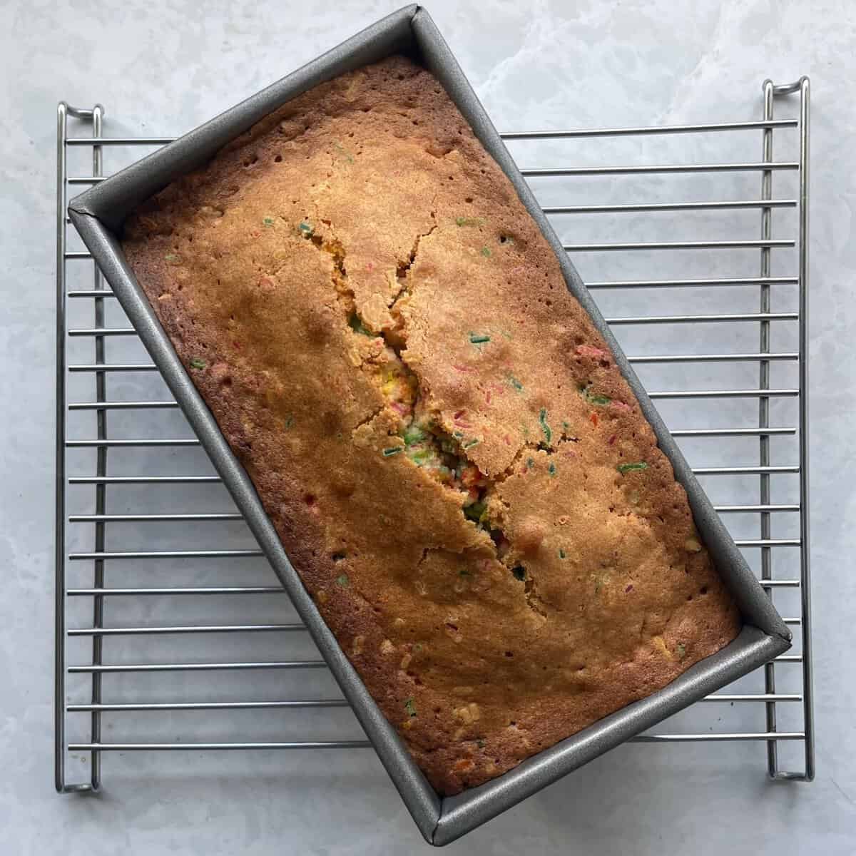 baked funfetti pound cake in the loaf pan on a cooling rack.