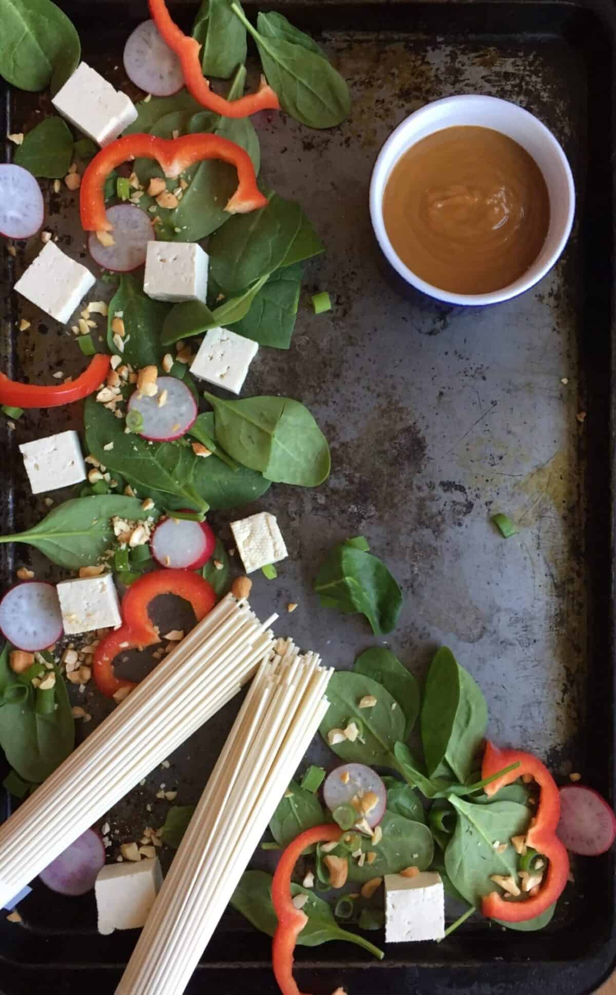 a sheet pan with tofu, noodles, spinach, peanuts, and red peppers.