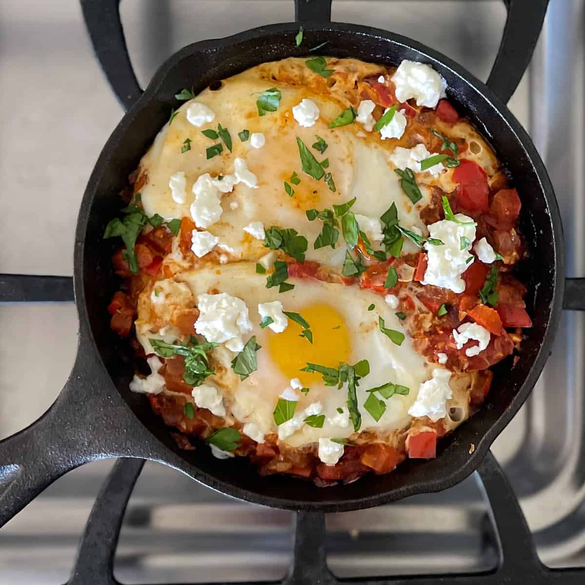 shakshuka for one person in small cast iron pan with eggs, feta, and herbs.