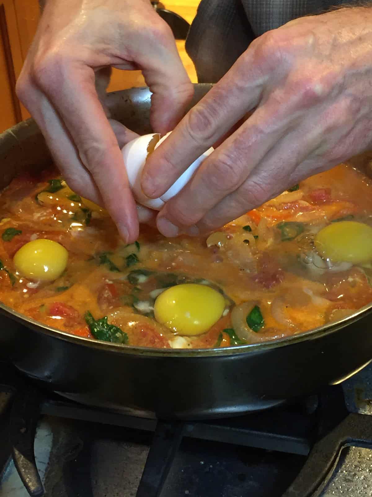 two hands showing how to crack eggs into the shakshuka pan.