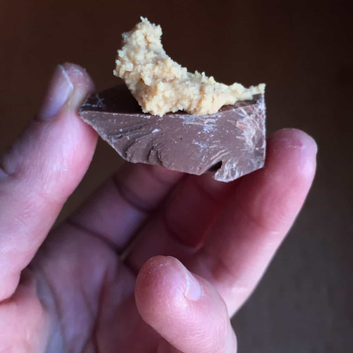 hand holding piece of bulk chocolate smeared with peanut butter bonbon filling.