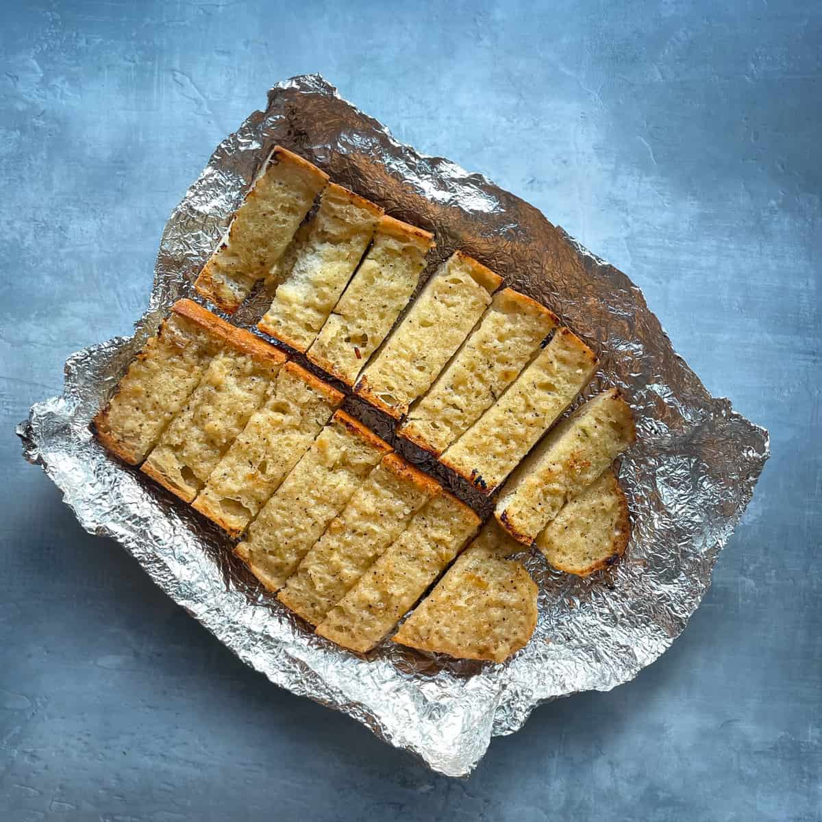 slices of two halves of a garlic bread baguette in aluminum foil.