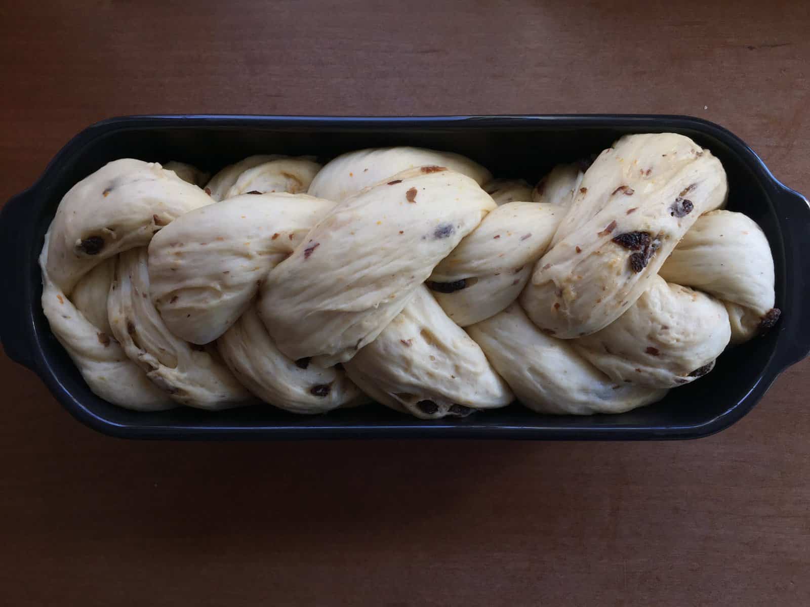 raisin challah after rising in a black ceramic loaf pan.