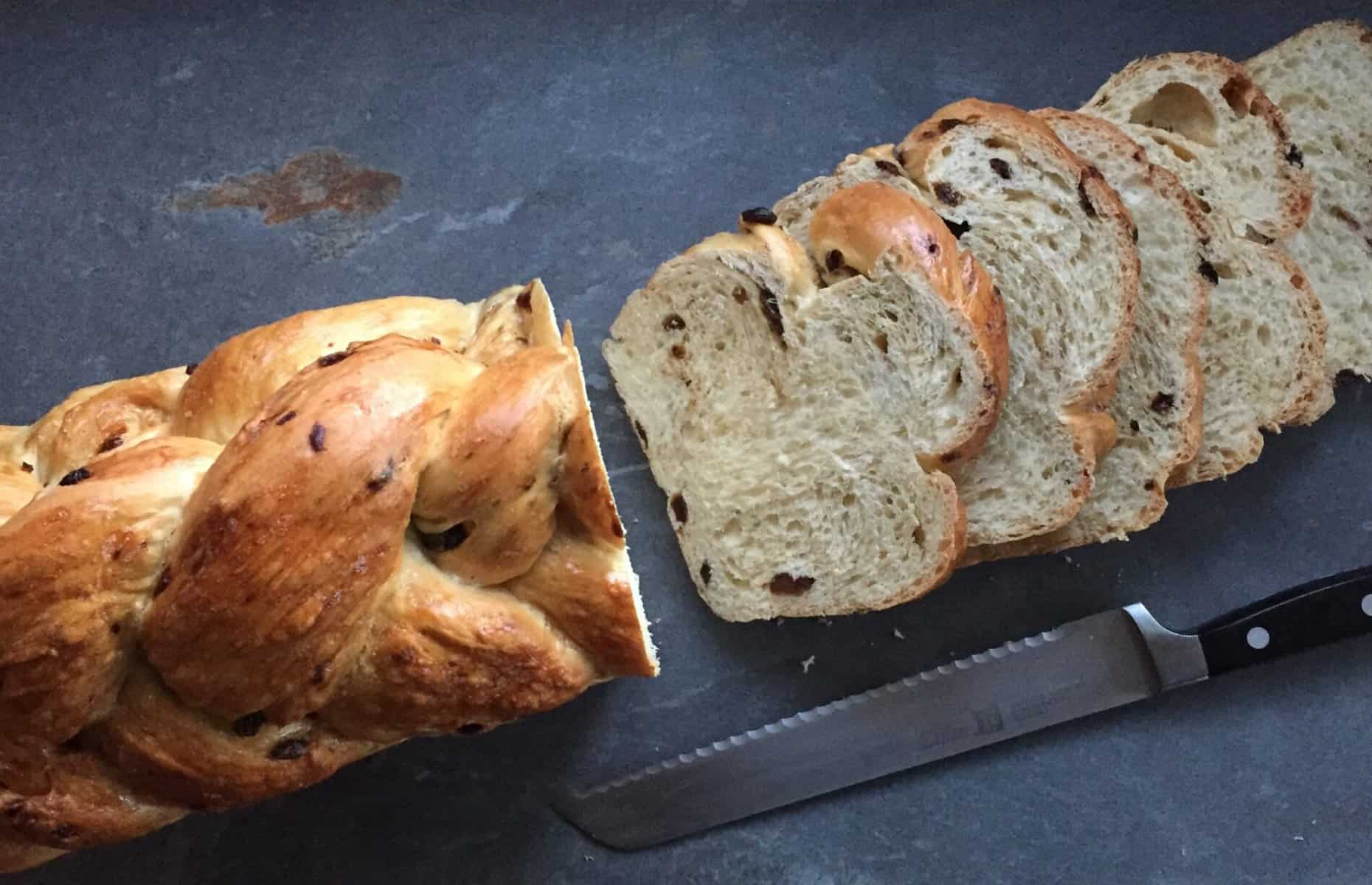 a 5 braid raisin challah with four slices and bread knife.