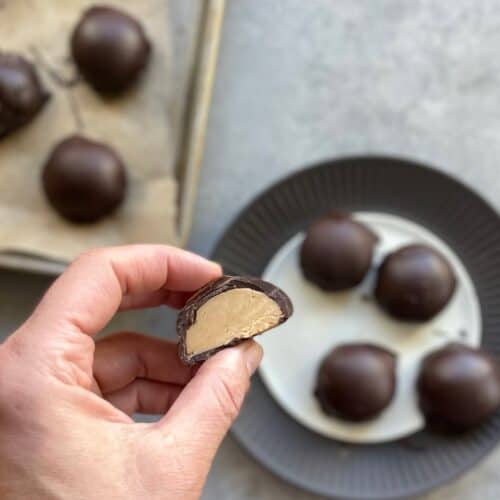 a hand holding half a chocolate peanut butter bonbon over a tray and plate of bonbons.