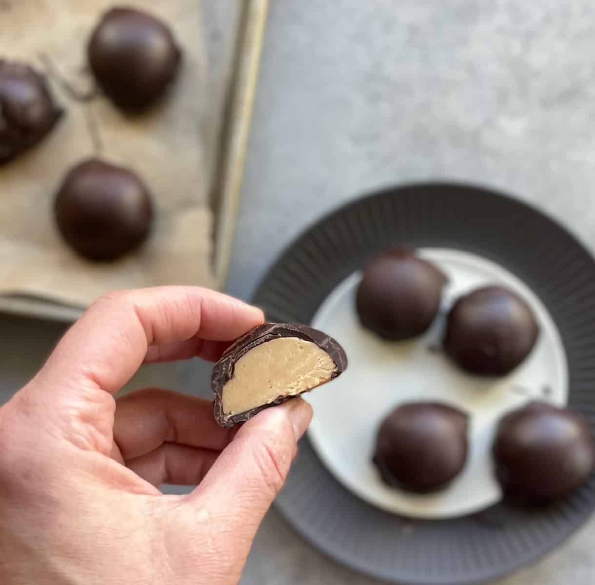 a hand holding half a chocolate peanut butter bonbon over a tray and plate of bonbons.