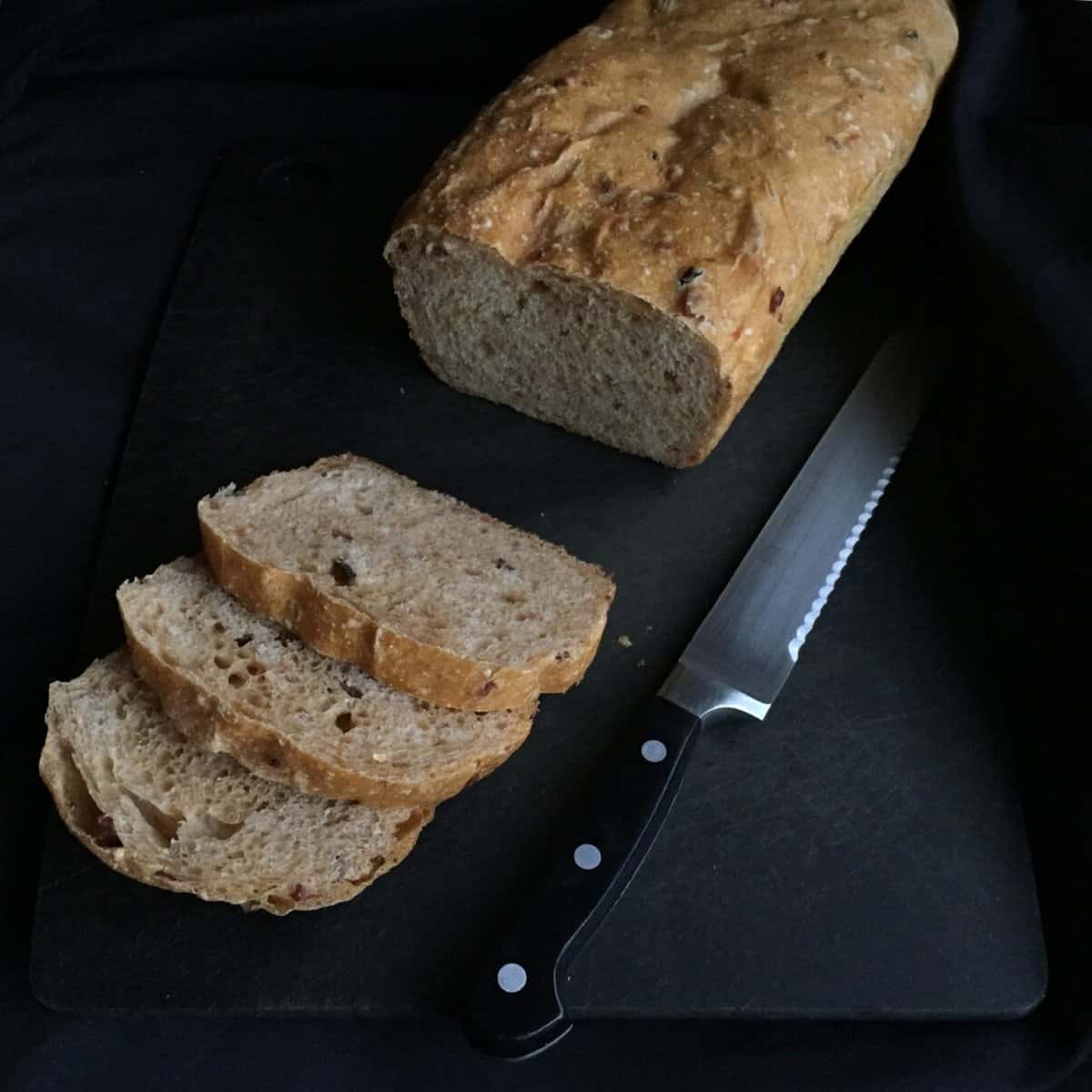 a loaf of bread on a dark background with three slices and a knife