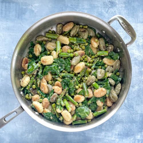 large frying pan with fried gnocchi, asparagus, peas, and spinach.
