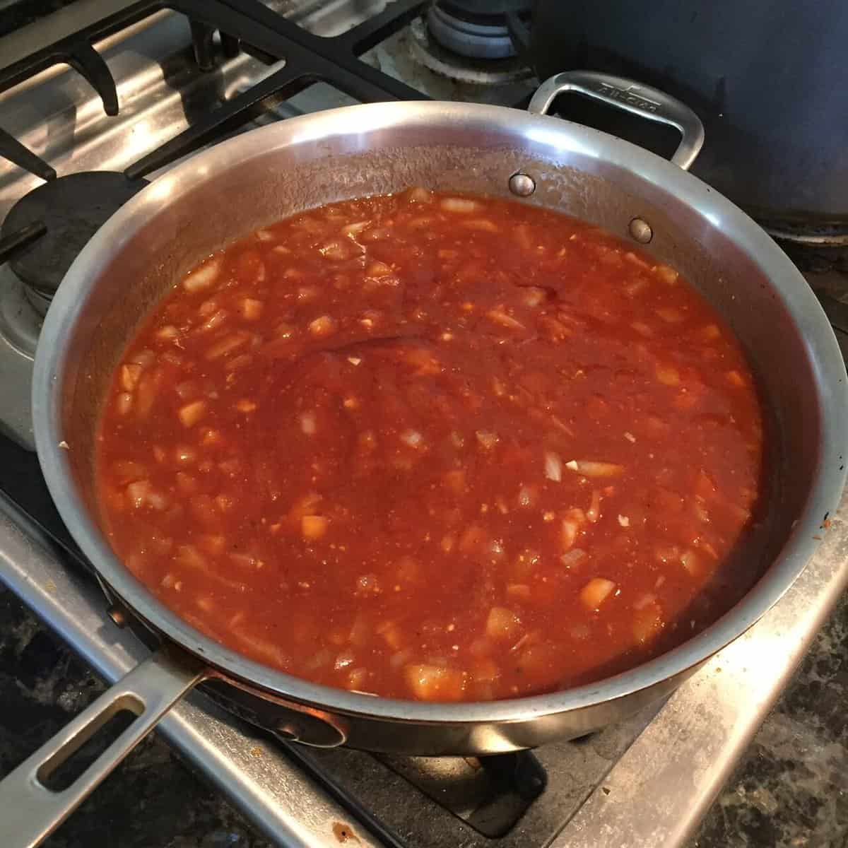 pan of barbecue sauce with bits of chopped onions on a stove top.