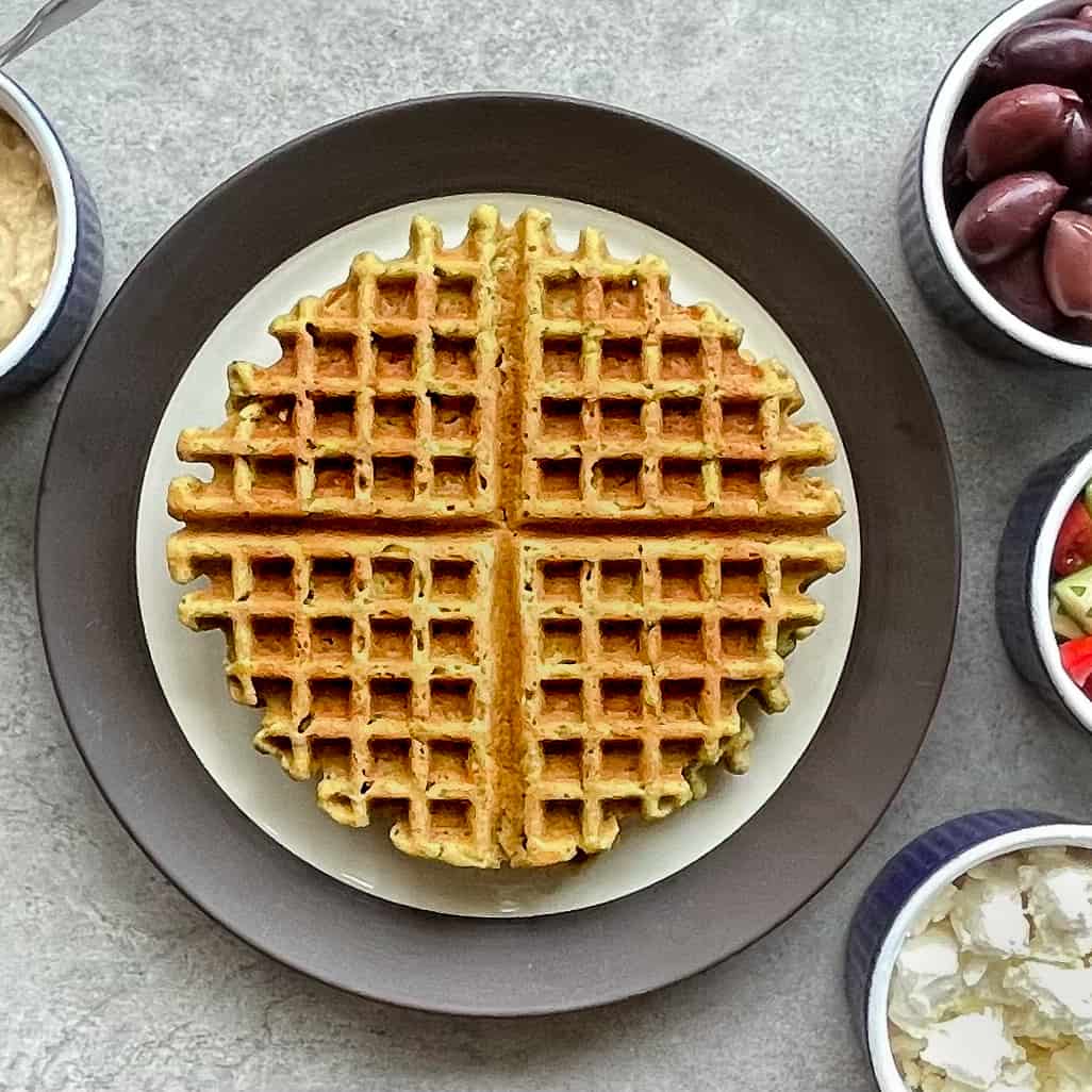 Waffled falafel on a plate with olives, feta, hummus, and tomato salad.