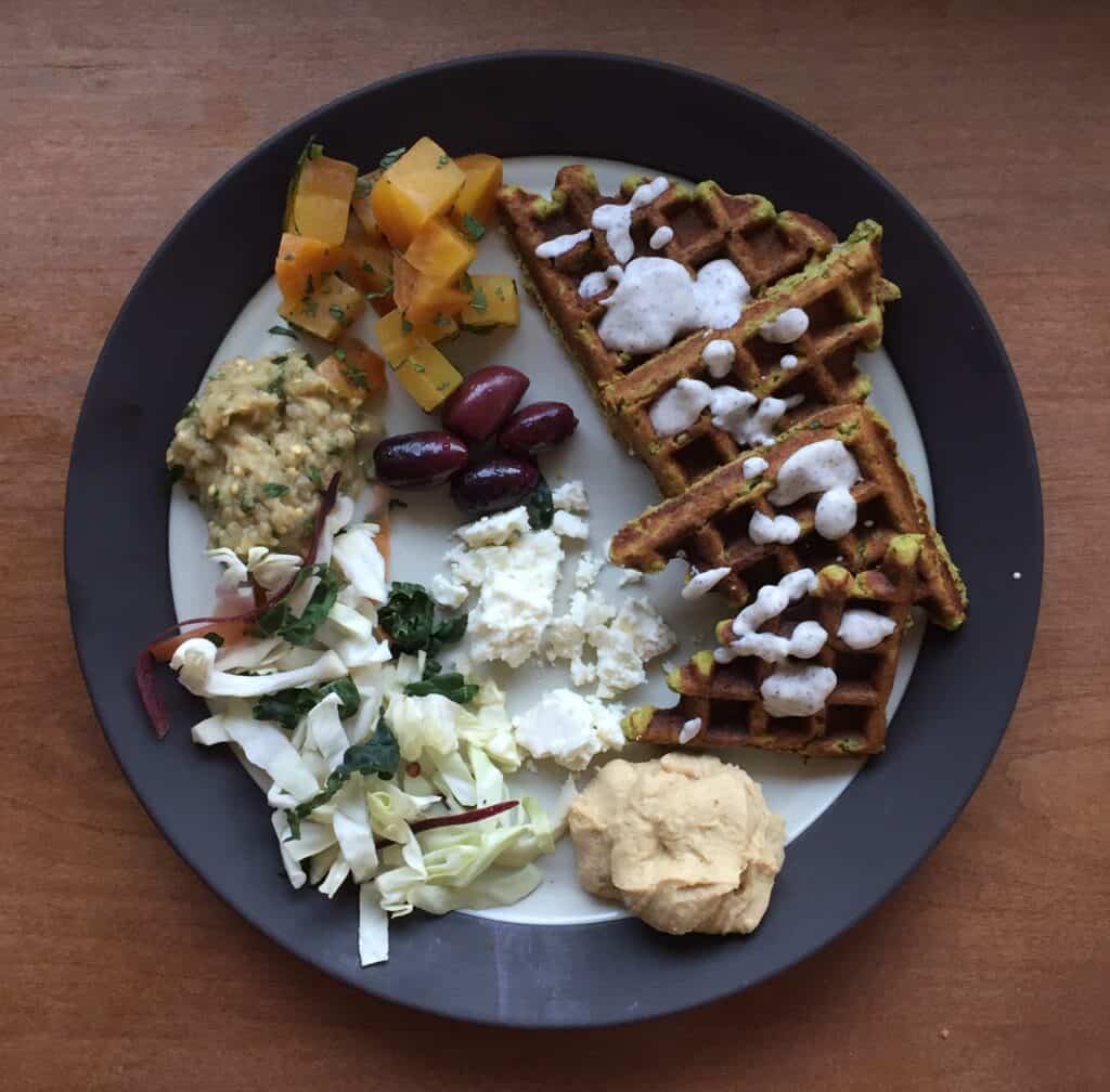 a plate of falafel waffle with hummus, baba ganoush, feta, olives, and roasted beets.