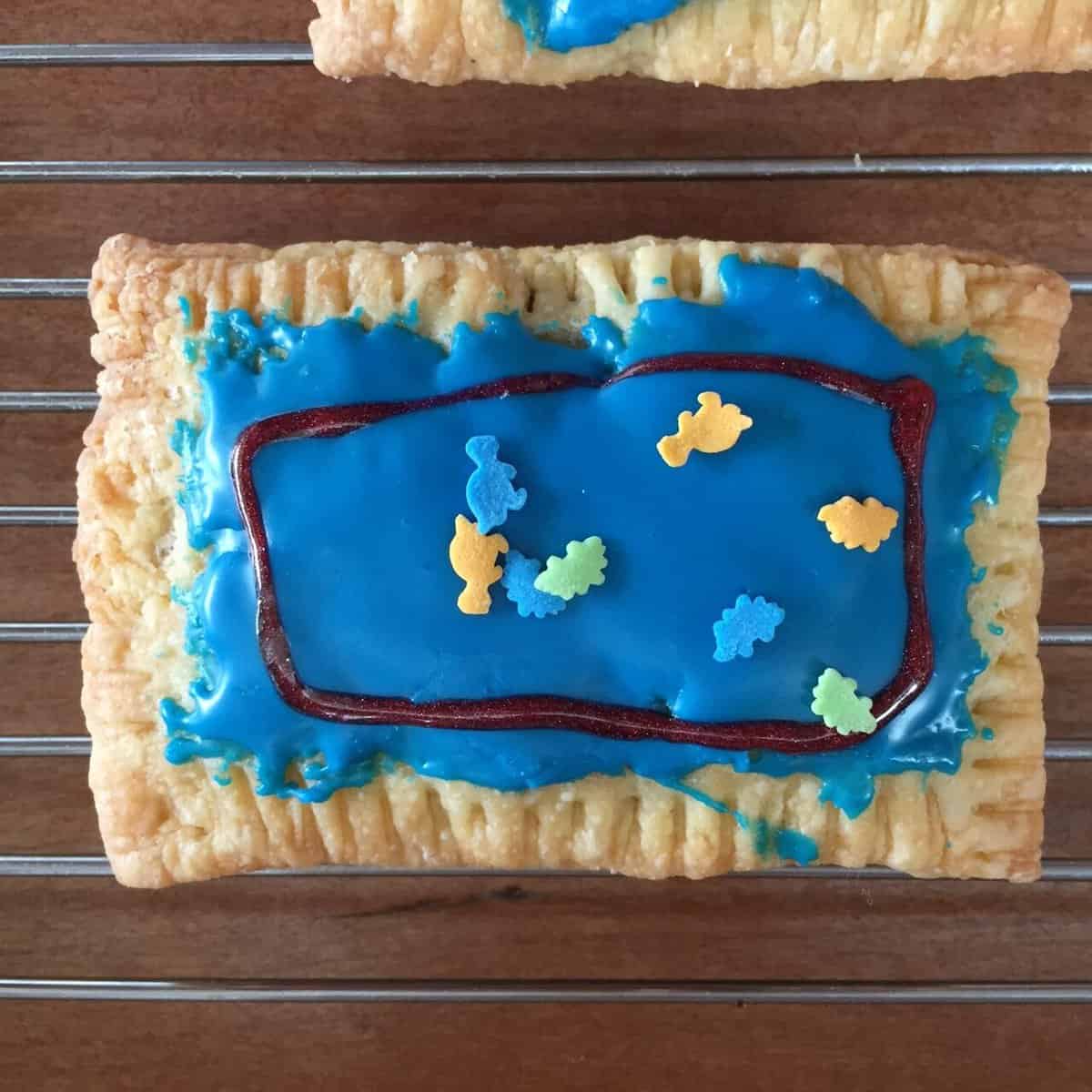 pop tart coated with blue frosting and decorated with dinosaur sprinkles.