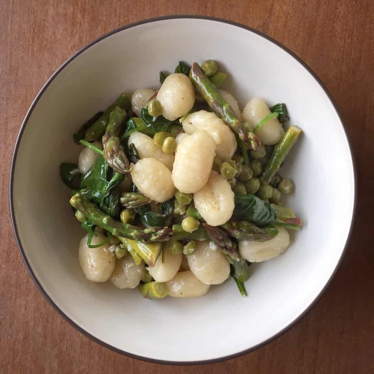 a bowl of gnocchi with asparagus, spinach, and peas