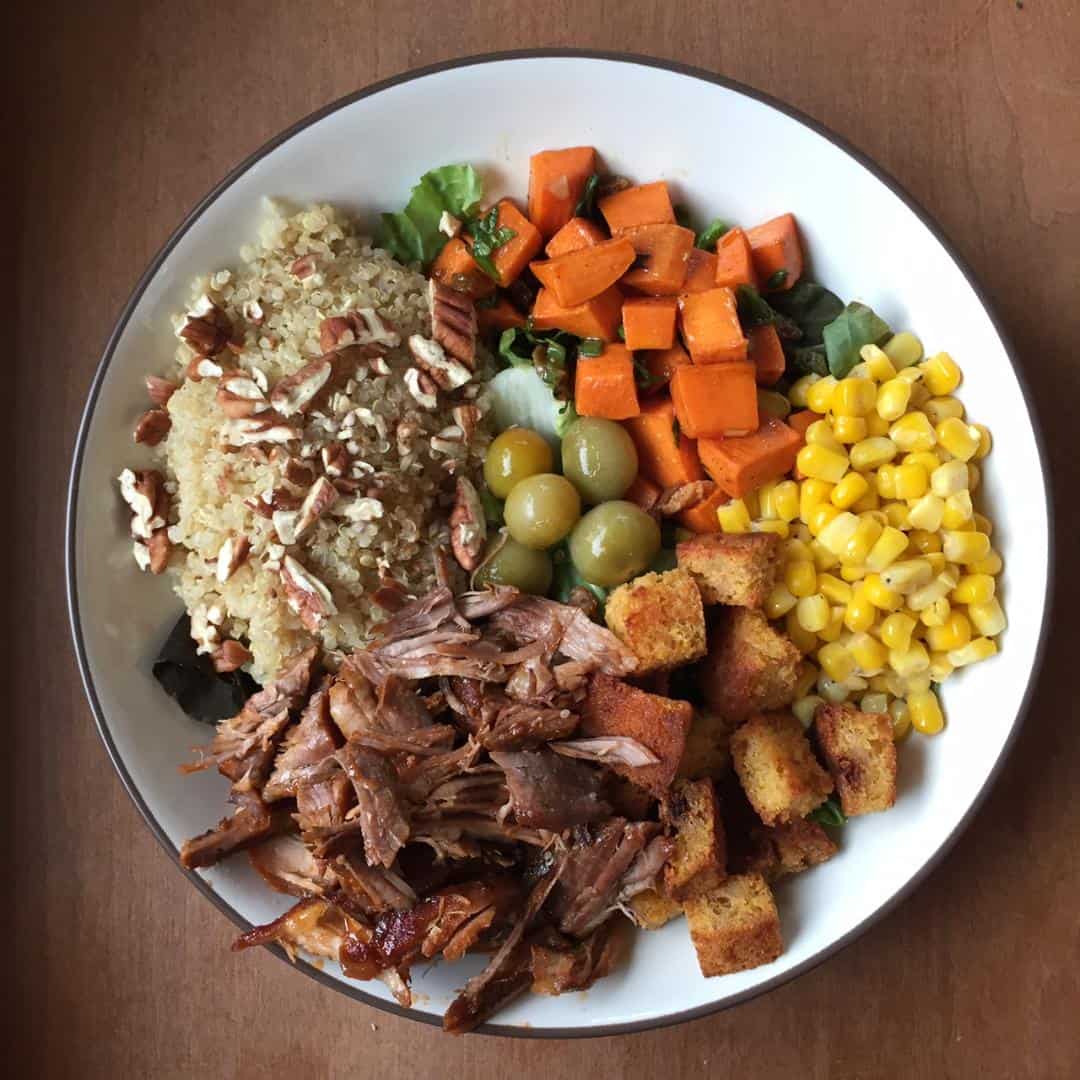 bowl with pulled pork, cornbread croutons, corn, sweet potato cubes, and quinoa topped with chopped pecans.