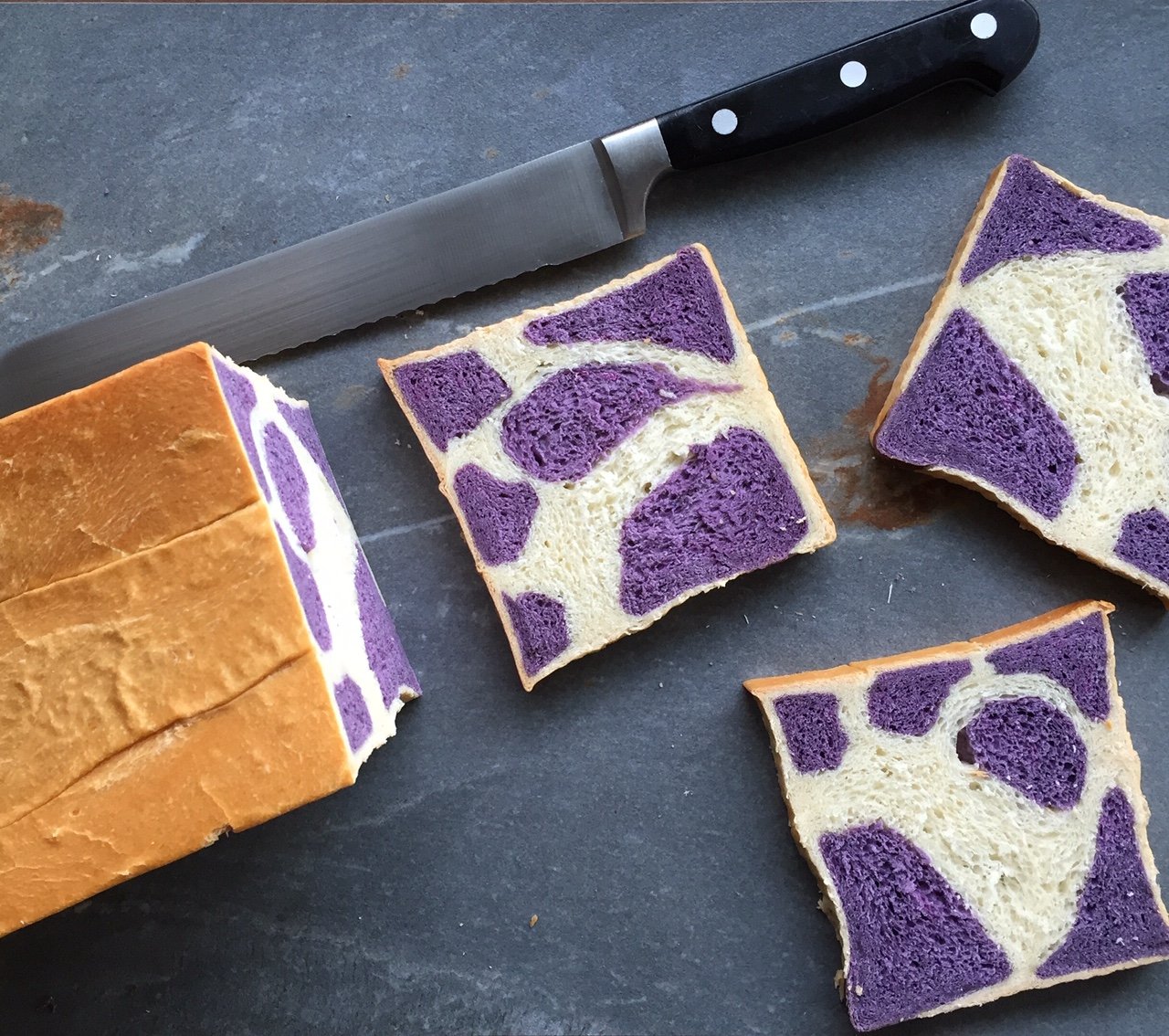 a loaf of bread with a purple cow pattern and three slices