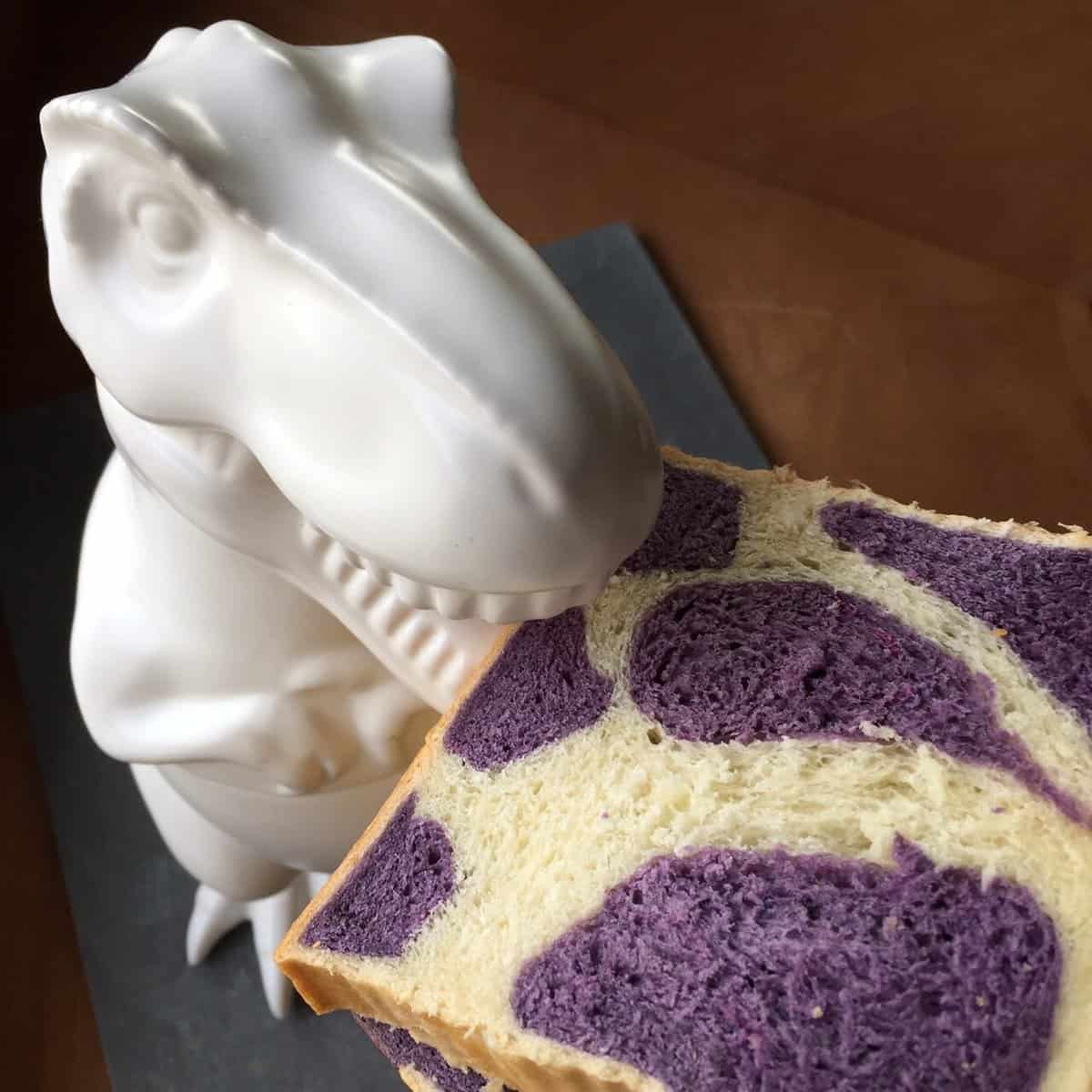 a dinosaur cookie jar eating a square slice of bread with a purple cow print.