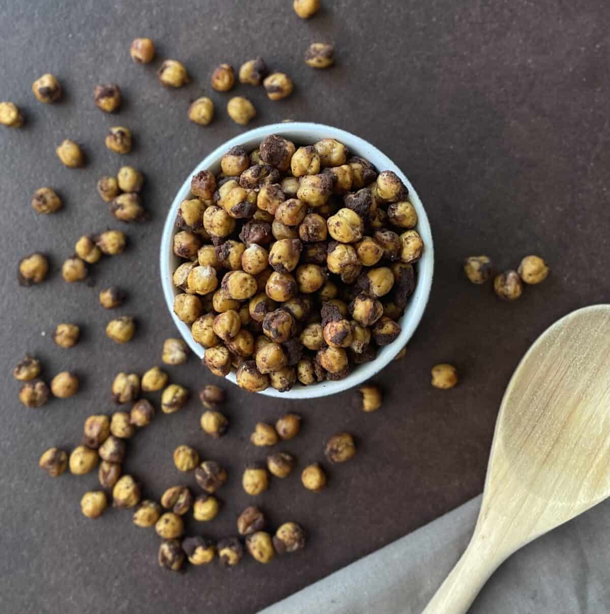 a small bowl of roasted chickpeas surrounded by more chickpeas and a wooden spoon.