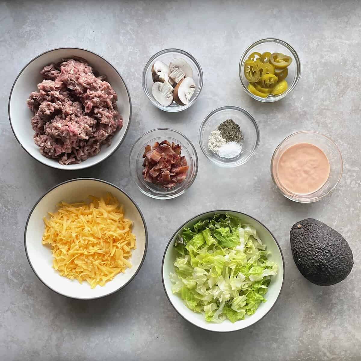 ground beef, shredded cheddar cheese, chopped bacon, avocado, mushrooms, pickles, salt, pepper, and spices, and campfire sauce.