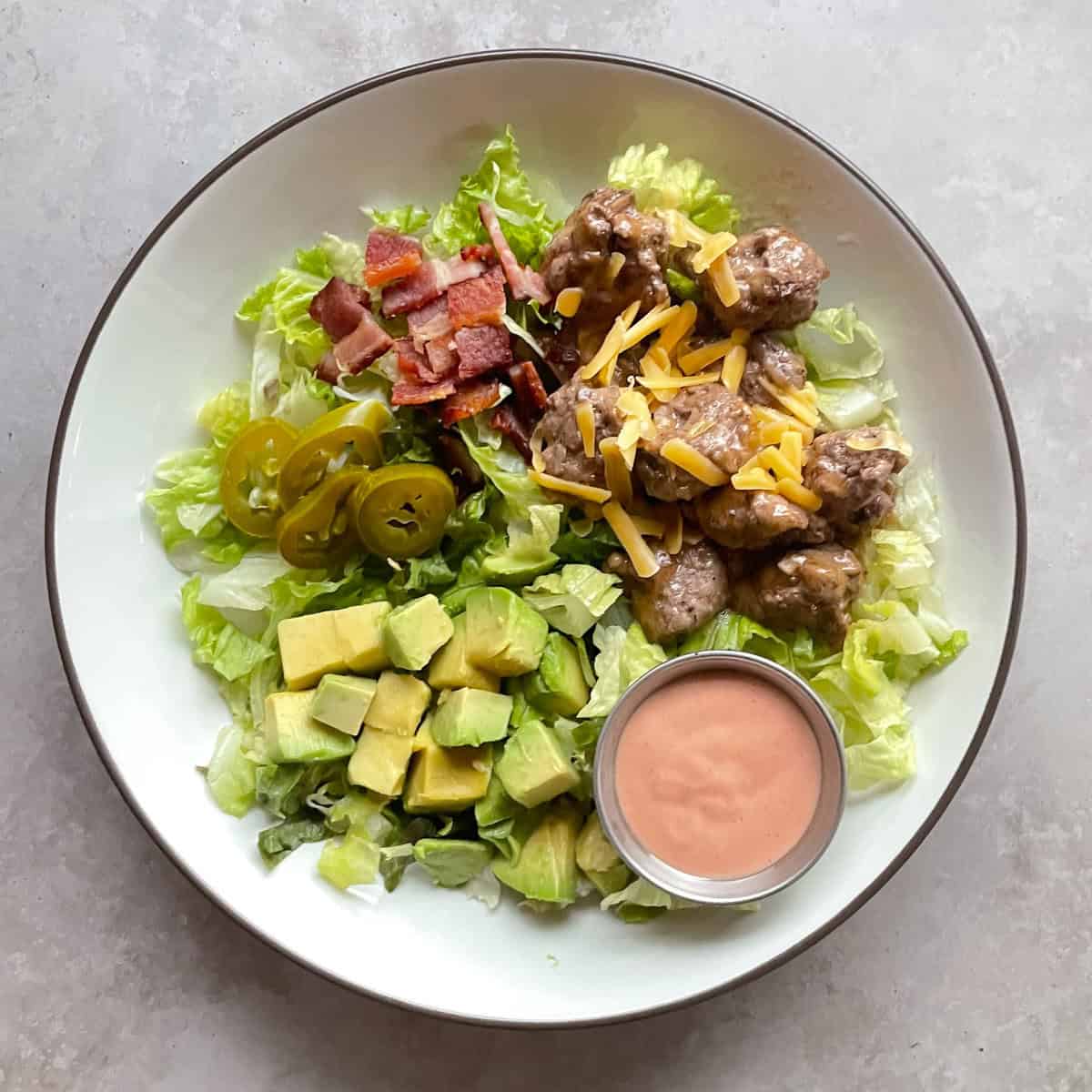 cheeseburger bowl with bacon, mini cheeseburgers, avocado, pickles, and ketchup dressing.