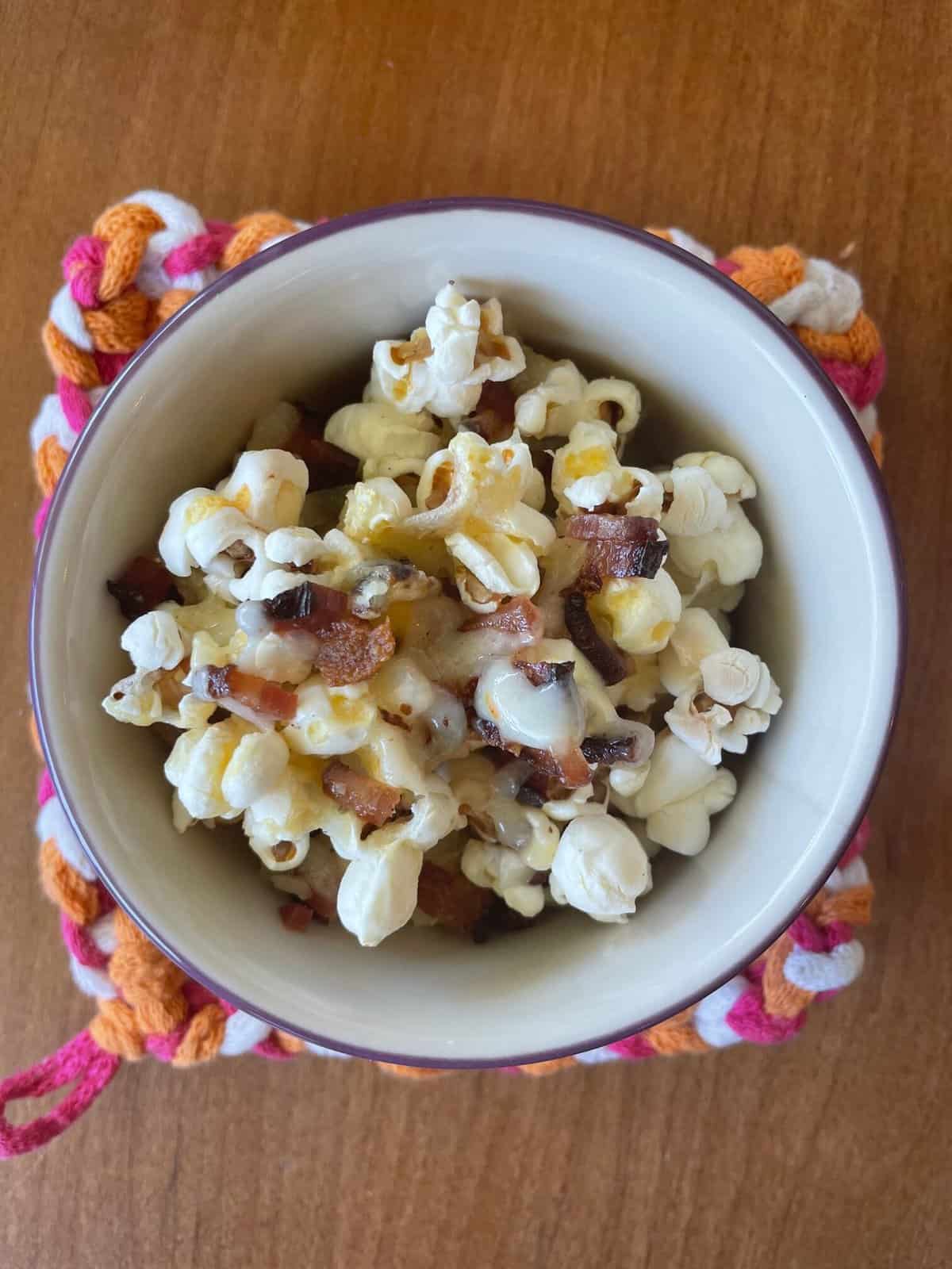 a small bowl of bacon cheddar popcorn on a colorful potholder.