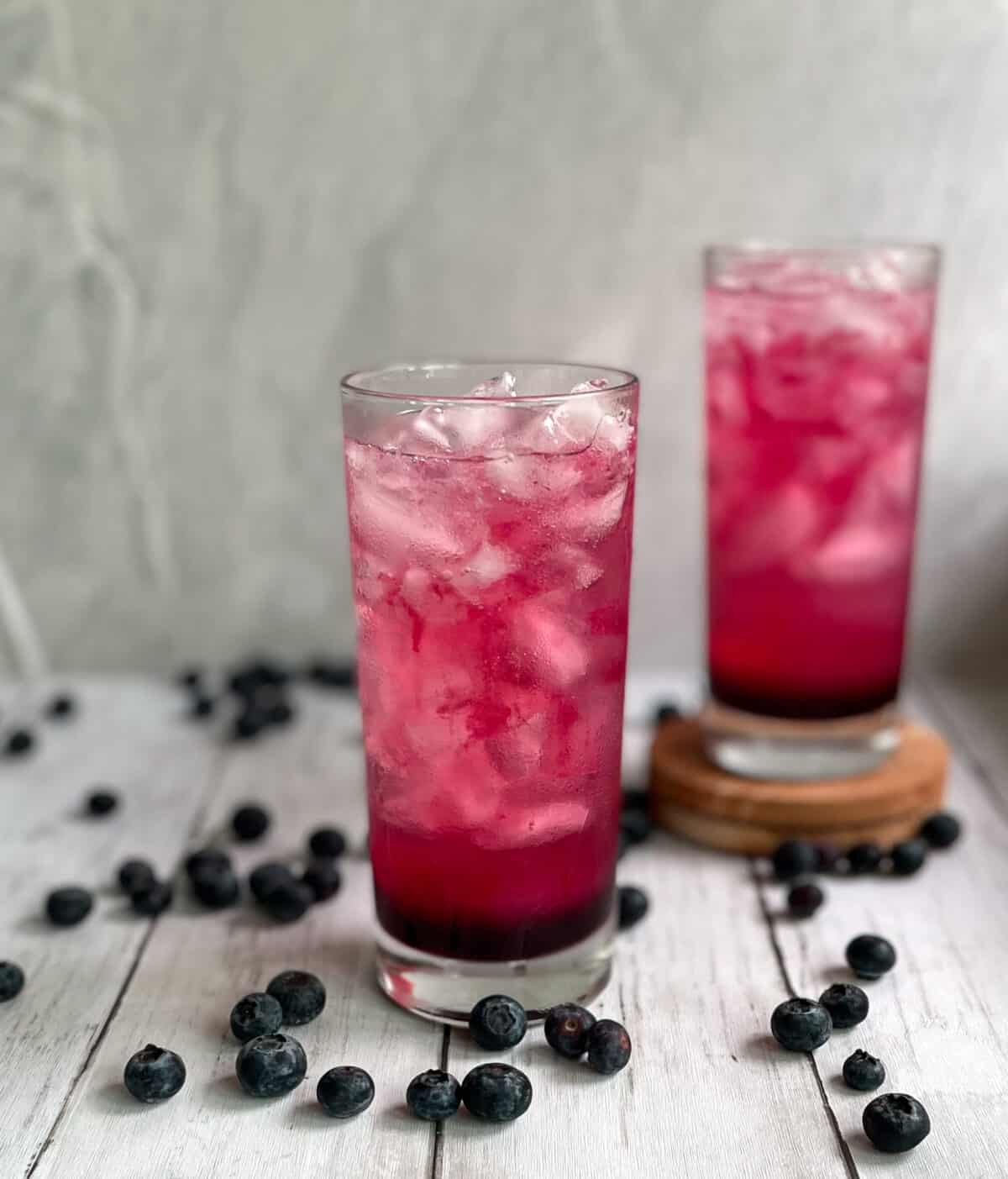 two deep pink blueberry gin and tonics surrounded by fresh blueberries.