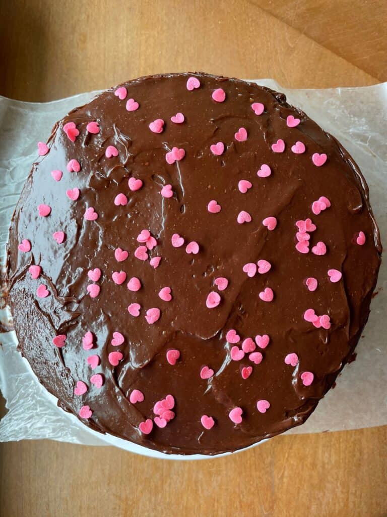 a chocolate cake decorated with chocolate ganache icing and pink candy hearts.