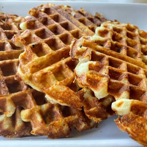 three ham and cheese waffles on a white plate.