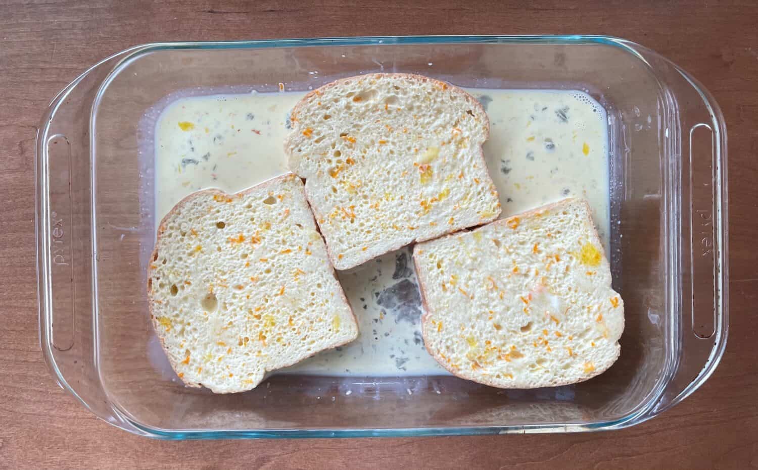 three slices of bread soaking up the orange zest French toast mixture.