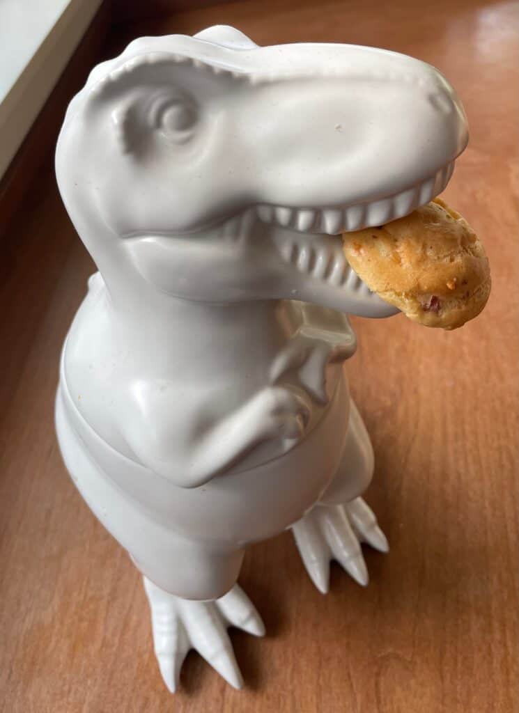 a dinosaur cookie jar eating a bacon and cheese puff.