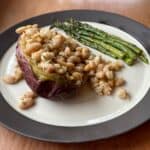 a plate with a baked purple sweet potato loaded with white beans and asparagus.