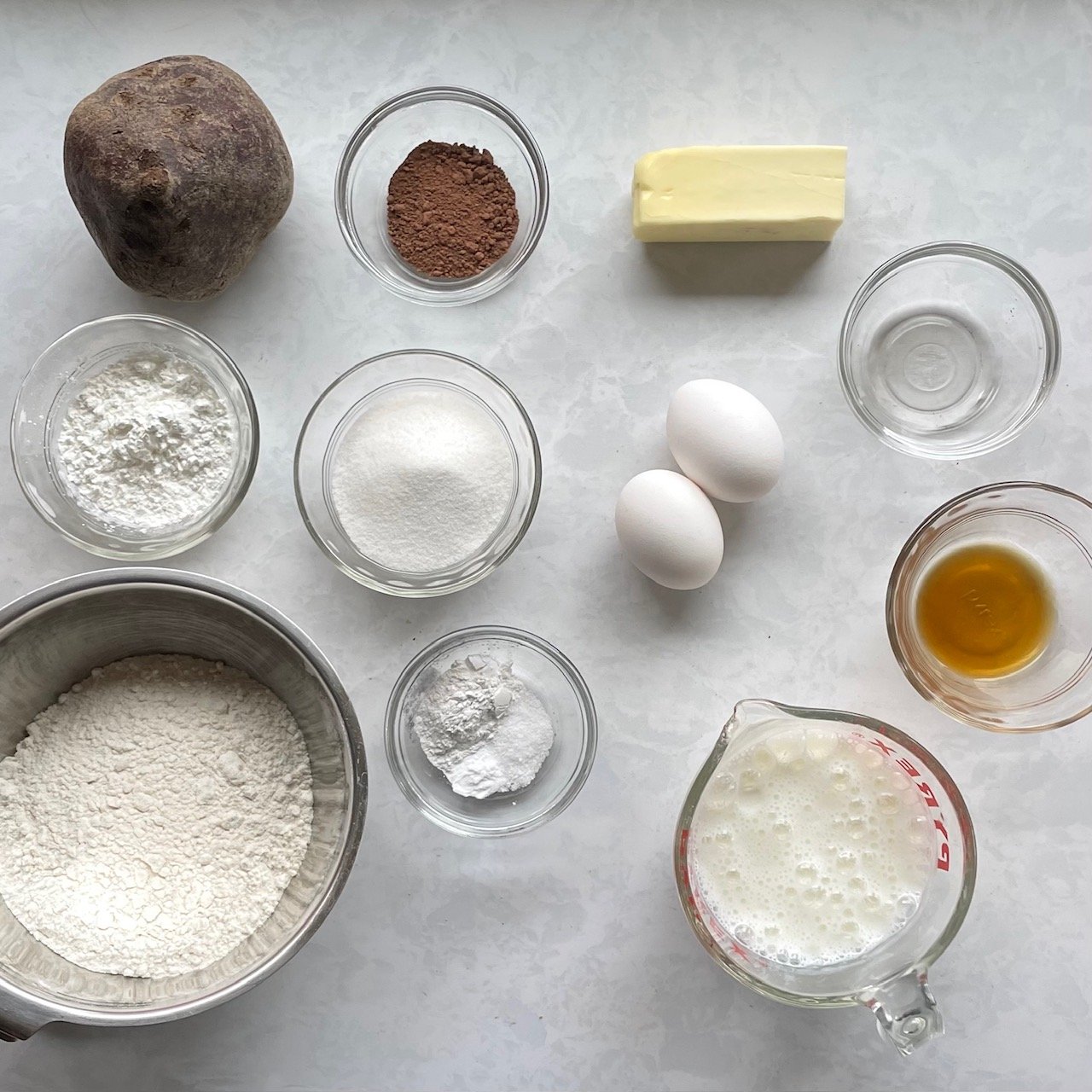 beet, egg, butter, flour, sugar, cocoa, vanilla, salt, and baking powder on a countertop.