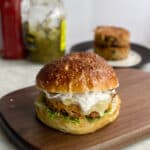 a cauliflower burger on a pretzel bun with cheese and lettuce with ketchup and relish in background.