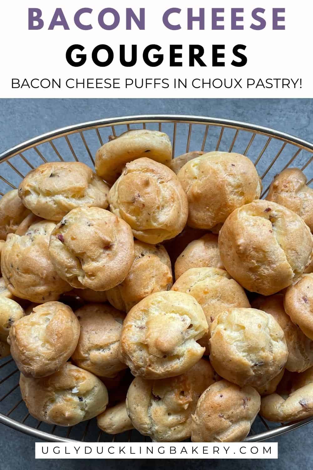 cheese bacon puffs filling up an oval wire bowl. The title says Bacon Cheese Gougeres. Bacon Cheese Puffs in Choux Pastry. The website ugly duckling bakery dot com is below.