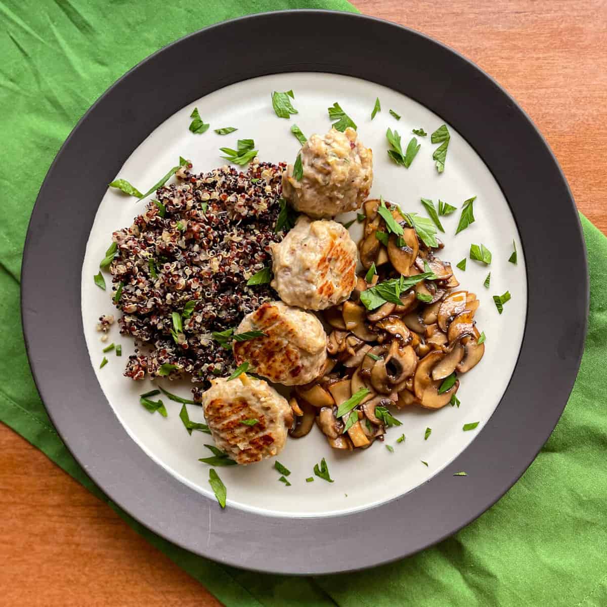 a plate of chicken and apple meatbals with quinoa, cooked mushrooms, and chopped parsley.