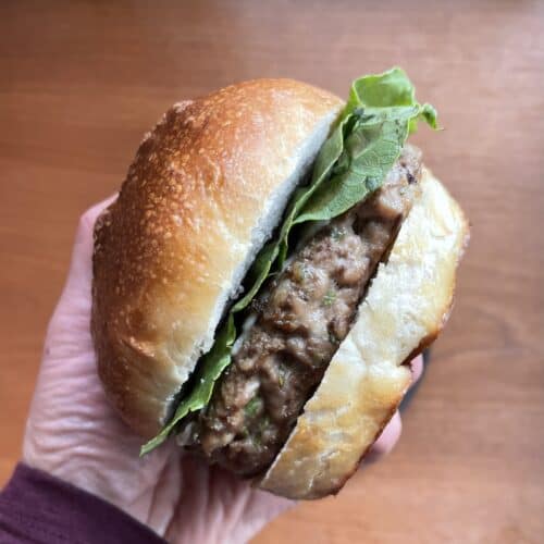 a duck burger with lettuce on a bun in someone's hand.