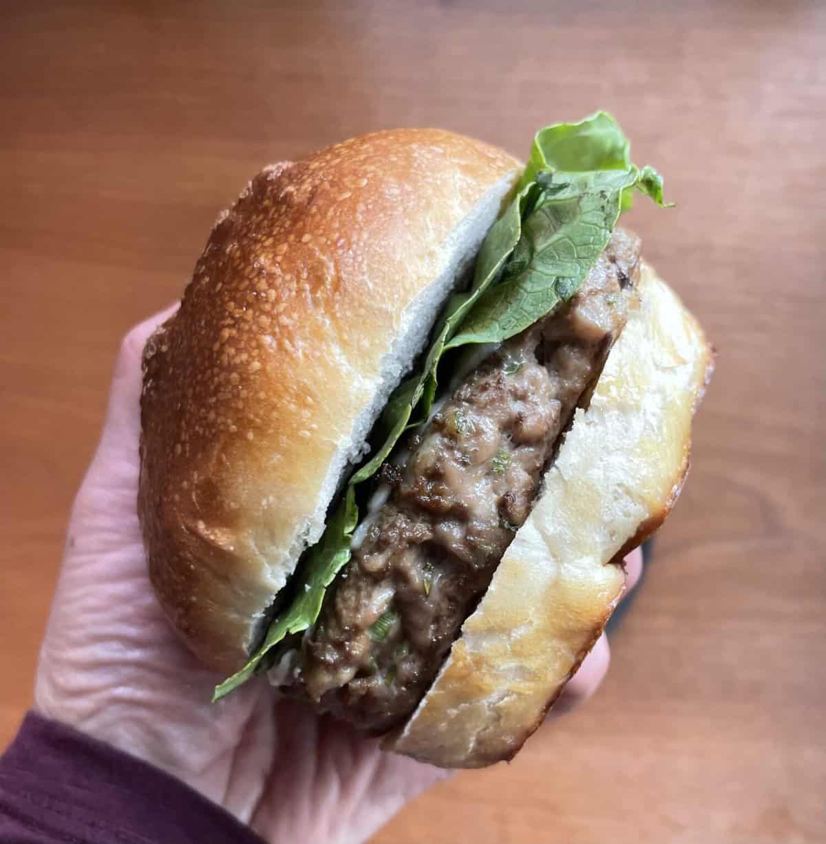 a duck burger with lettuce on a bun in someone's hand.