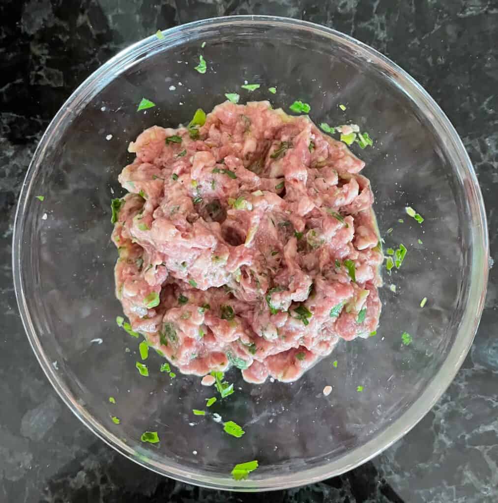 a glass bowl filled with the raw duck burger mixture.