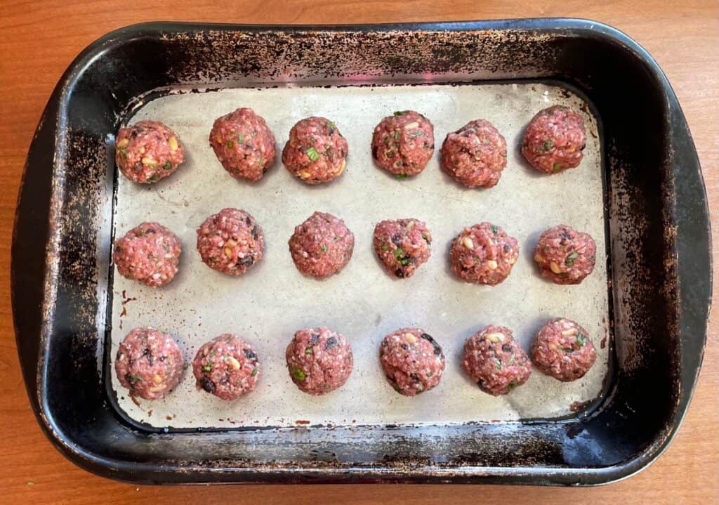 a roasting pan with uncooked lamb, raisin, and pine nut meatballs.