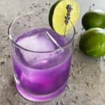 a purple lavender gimlet in a lowball glass garnished with lime and lavender.