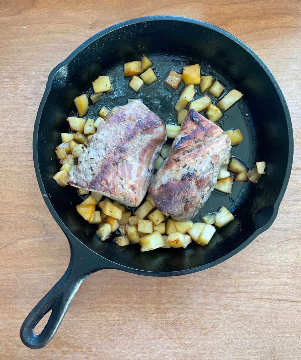 a cast iron pan with a cooked pork tenderloin over chopped apples