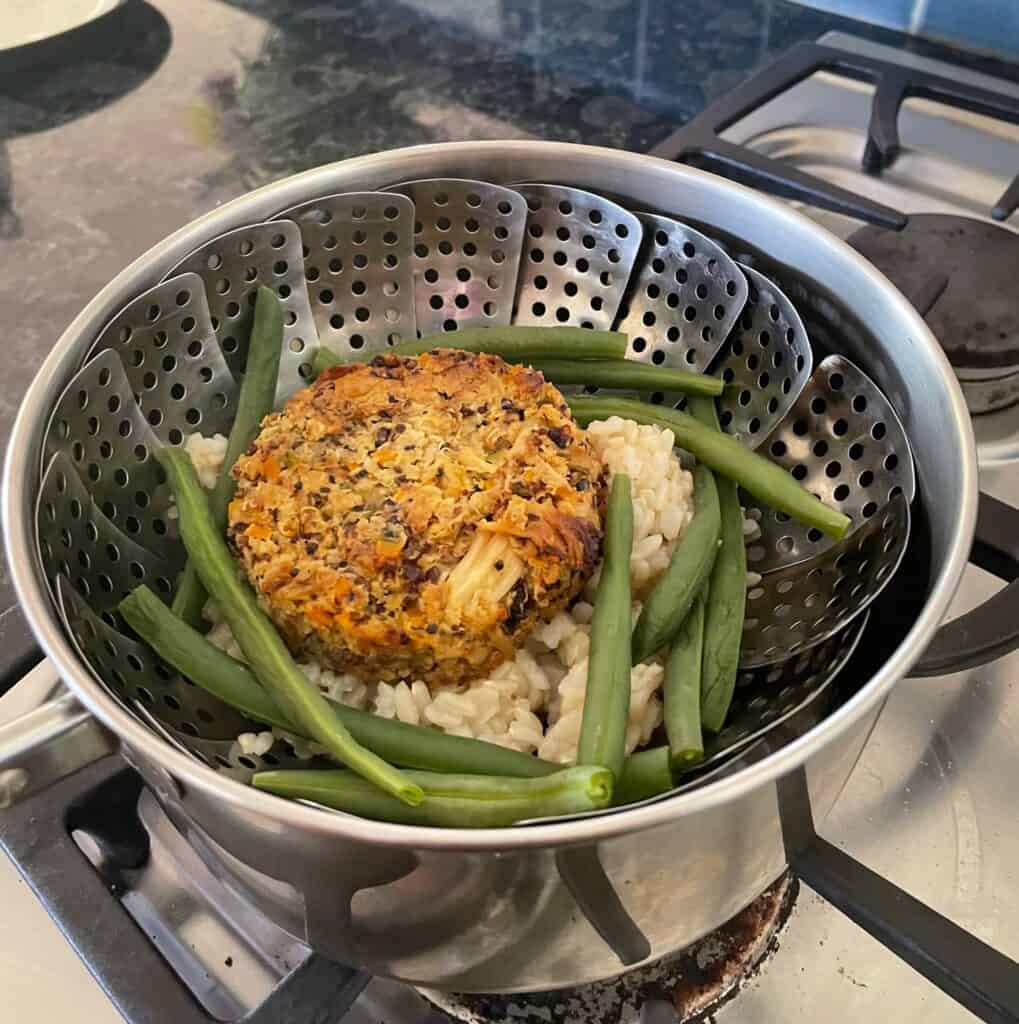 steamer basket with a baked cauliflower patty, green beans, and brown rice.