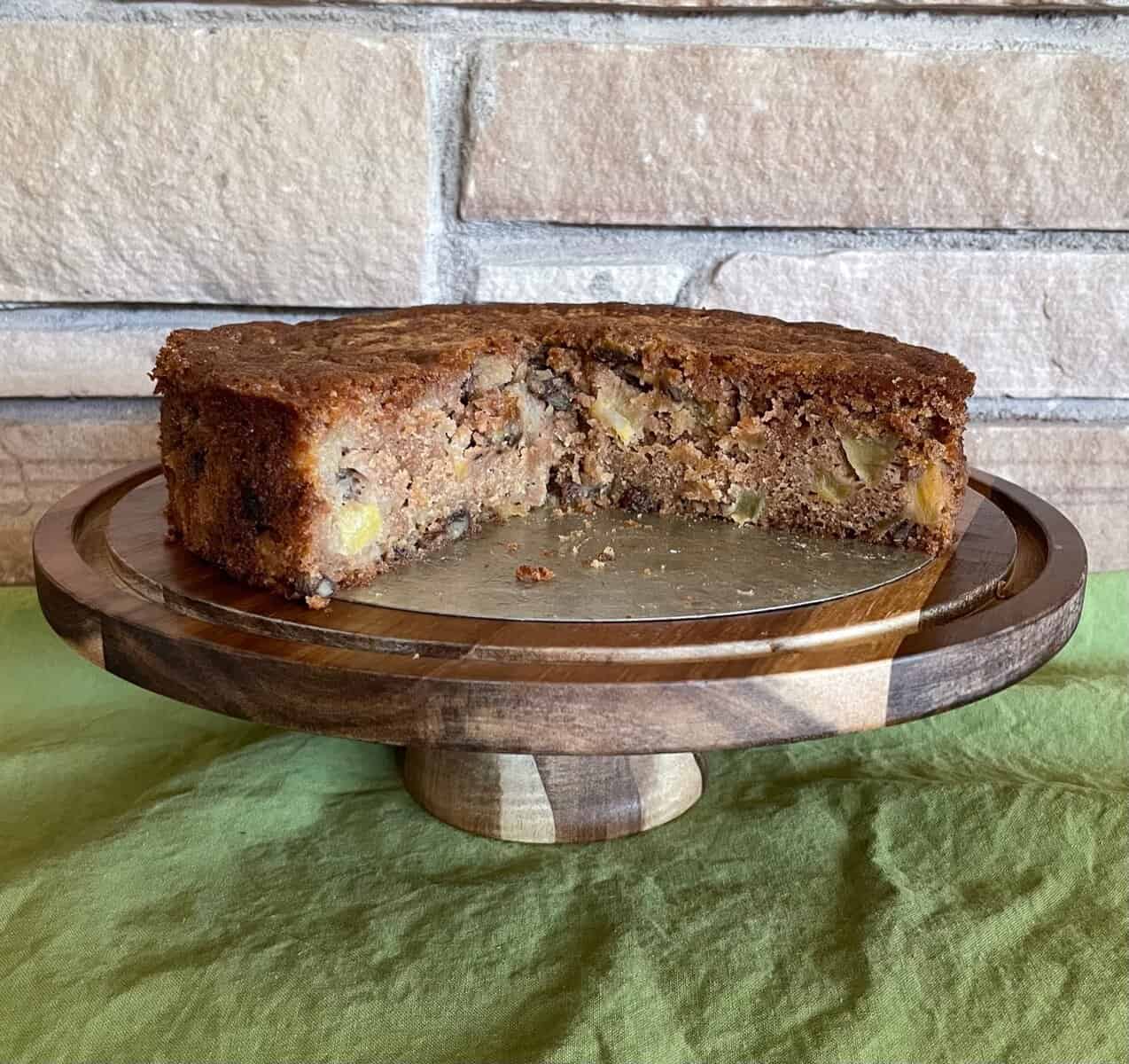 three quarters of a sourdough discard apple cake on a wood cake stand