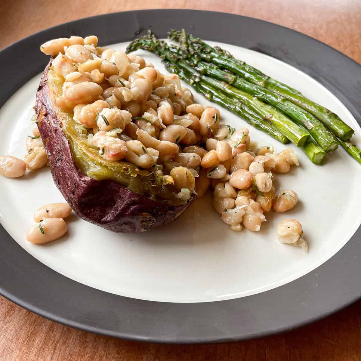 twice baked purple sweet potato loaded with cheesy white beans on a plate with asparagus.
