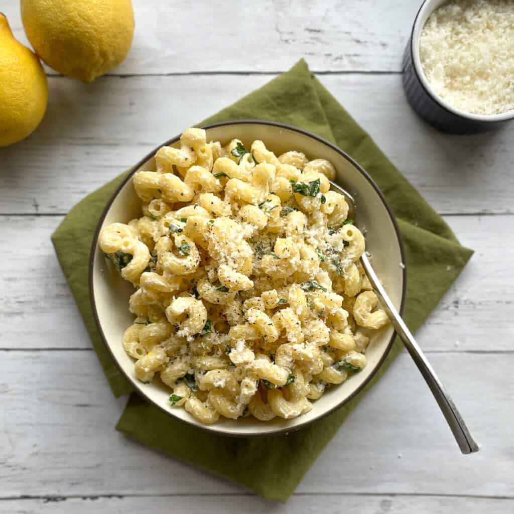 a bowl of cavatappi with a lemon ricotta sauce, two lemons, and small bowl of Parmesan.